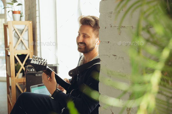 Caucasian musician playing guitar during online concert at home isolated and quarantined, cheerful