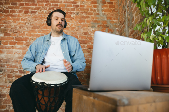 Caucasian musician playing hand drum during online concert at home isolated and quarantined