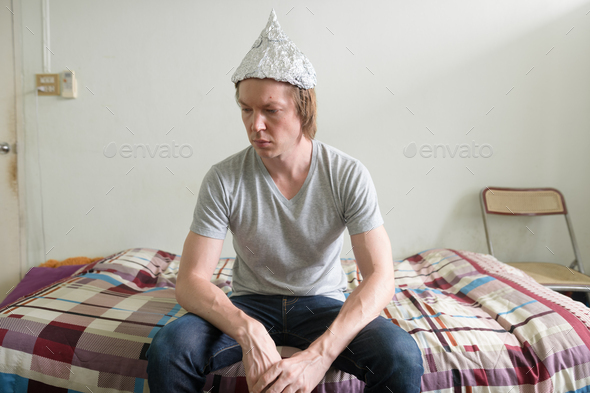 Stressed young man with tin foil hat thinking in the bedroom