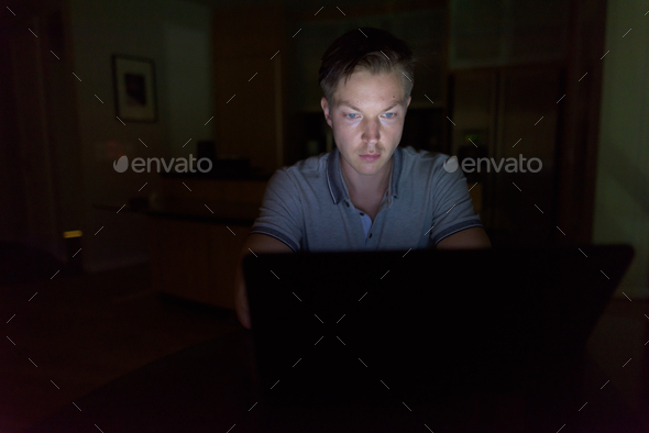 Young handsome man using laptop in the dark living room