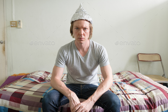 Young man with tin foil hat in the bedroom