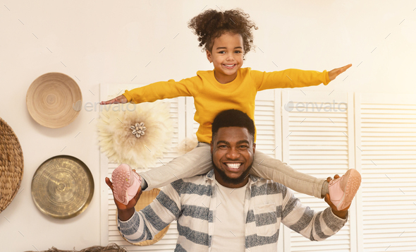 African american dad holds daughter on shoulders and flies like plane
