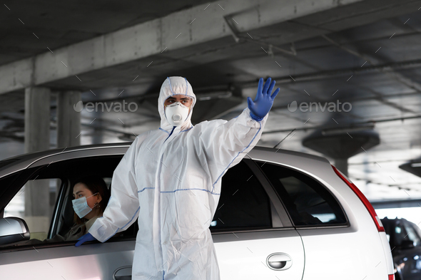Man in protective suit showing stop sign, woman in car is sick with coronavirus