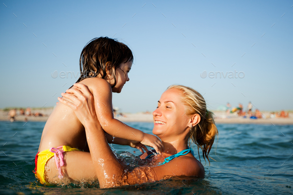 Young mother standing in water and helping to swim her small daughter