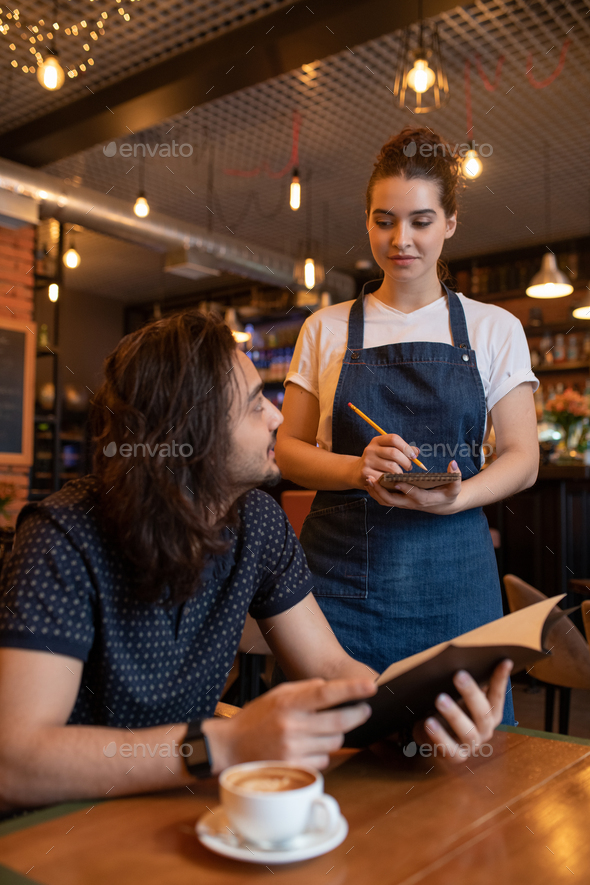 Young client sitting in restaurant, looking through menu and ordering lunch