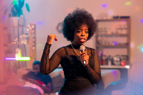 Young elegant woman in elegant black dress singing karaoke in microphone