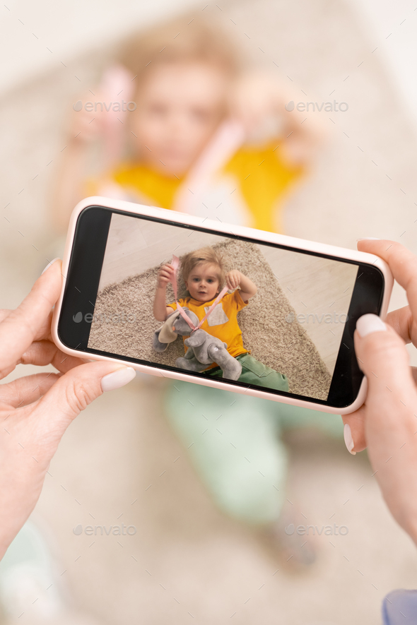 Young female hands with smartphone making video or phone of her cute son