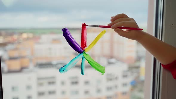 Child draw snowflake in rainbow colours on window with paints. Caucasian female person decorate room alt