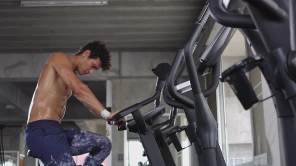 Topless athlete man cardio riding on bicycle at the gym