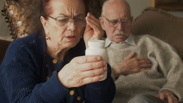 An elderly man gets sick and his wife reads a pills instruction. Senior couple take pill medicine fo