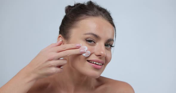 Young Woman Putting Cream on Her Chick and Laughing to Camera Pretty Female Model Using Cosmetics alt