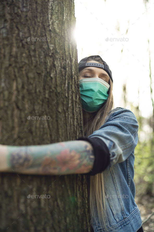 Casual Woman Hugging Tree in Park Wearing Face Protection Mask Against Coronavirus