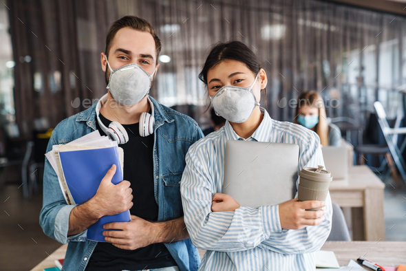 Photo of multinational students in medical masks standing at classroom