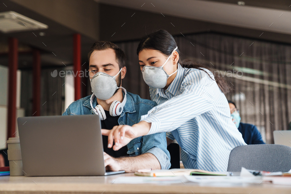 Photo of young students in medical masks studying with laptop