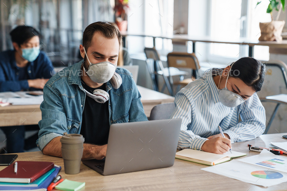 Photo of multinational students in medical masks studying with laptop