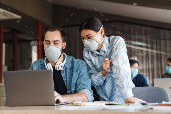 Photo of joyful students in medical masks studying with laptop