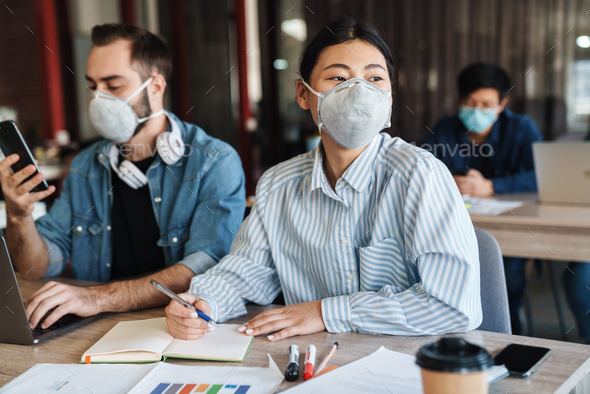 Photo of students in medical masks studying with laptop and cellphone