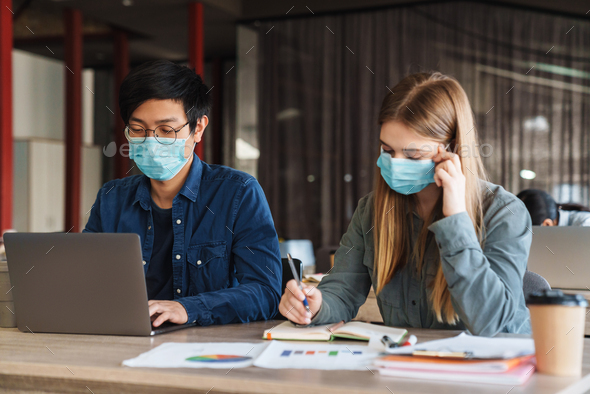 Photo of young students in medical masks studying with laptop