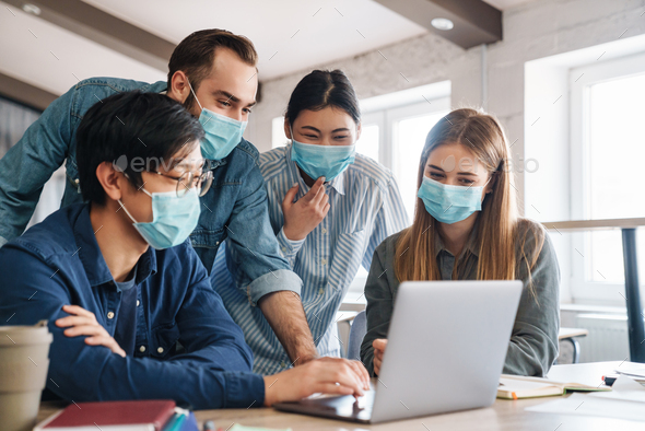 Photo of pleased students in medical masks studying with laptop