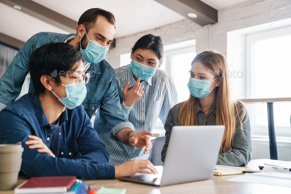 Photo of multinational students in medical masks studying with laptop