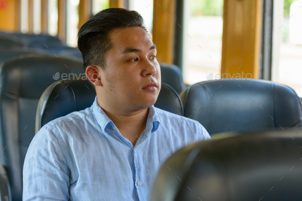 Young overweight Asian tourist man riding inside the train