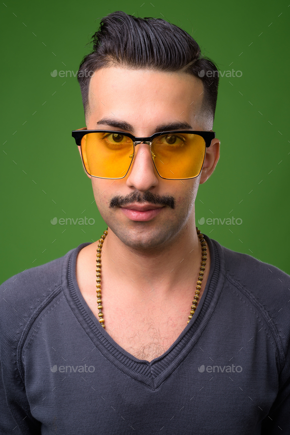 Young handsome Iranian man with mustache against green backgroun