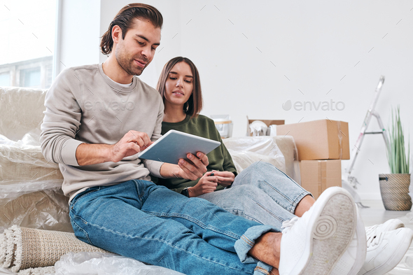 Young man in casualwear surfing in the net while looking for new furniture