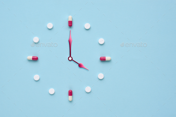 Clock created from pills and capsules on pastel blue background