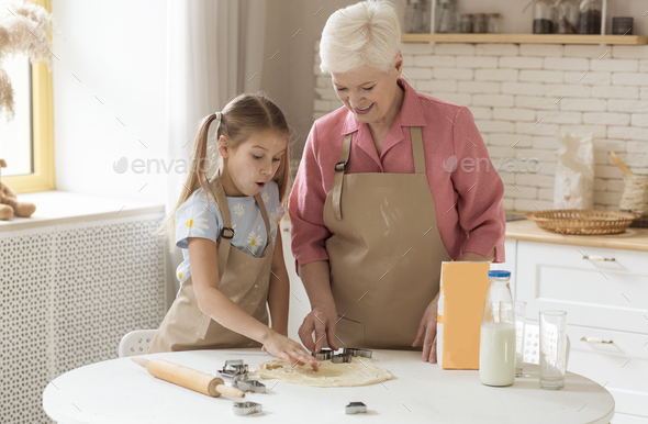 Grandma with her cute little granddaughter making cookies in sunny kitchen