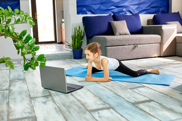 Little cute girl in sportswear on blue mat practicing gymnastics at home