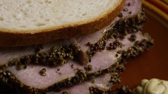 Rotating shot of delicious, premium pastrami sandwich next to a dollop of dijon mustard alt