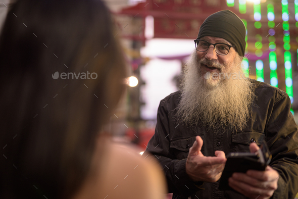 Friendly mature bearded tourist man asking directions from young woman in Chinatown at night