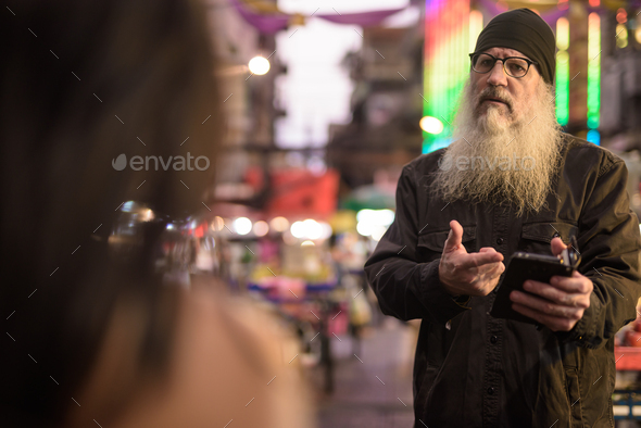 Mature bearded tourist man asking directions from young woman in Chinatown at night