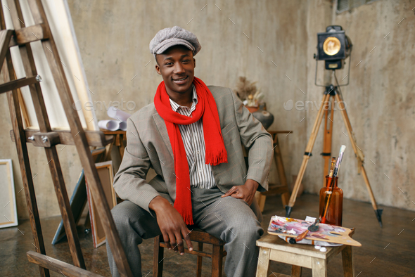 Painter in hat and red scarf poses at easel