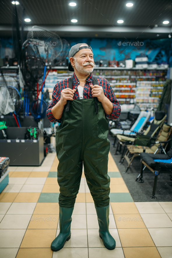 Fisherman tries on rubber jumpsuit in fishing shop Stock Photo by NomadSoul1