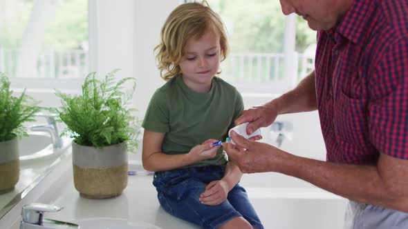 Caucasian grandfather helping his grandson to apply toothpaste on toothbrush at home alt