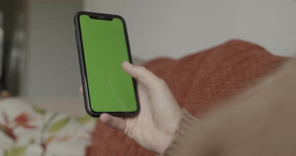 Close up of green screen on smart phone with woman sitting on sofa at home