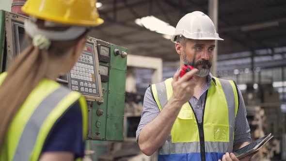 Male engineer foreman talking on walkie talkie to colleagues while training female trainee