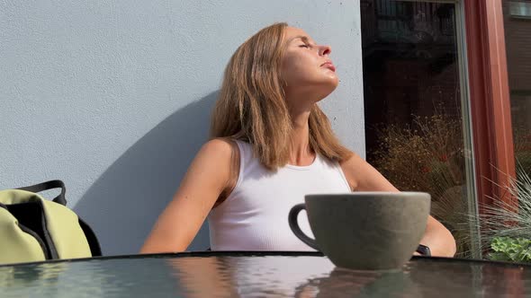 Low angle view at a woman drinking tea or coffee on outdoor terrace in hot sunny day, she