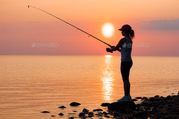 Woman fishing on Fishing rod spinning at sunset background. Stock