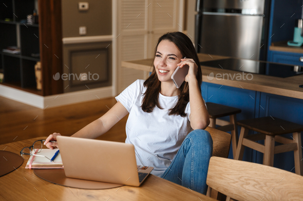 Image of smiling woman talking on cellphone and working with laptop