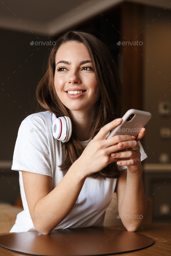 Image of smiling woman with wireless headphones using cellphone