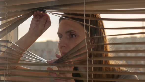 Woman Looking Outside Through Open Window Blinds