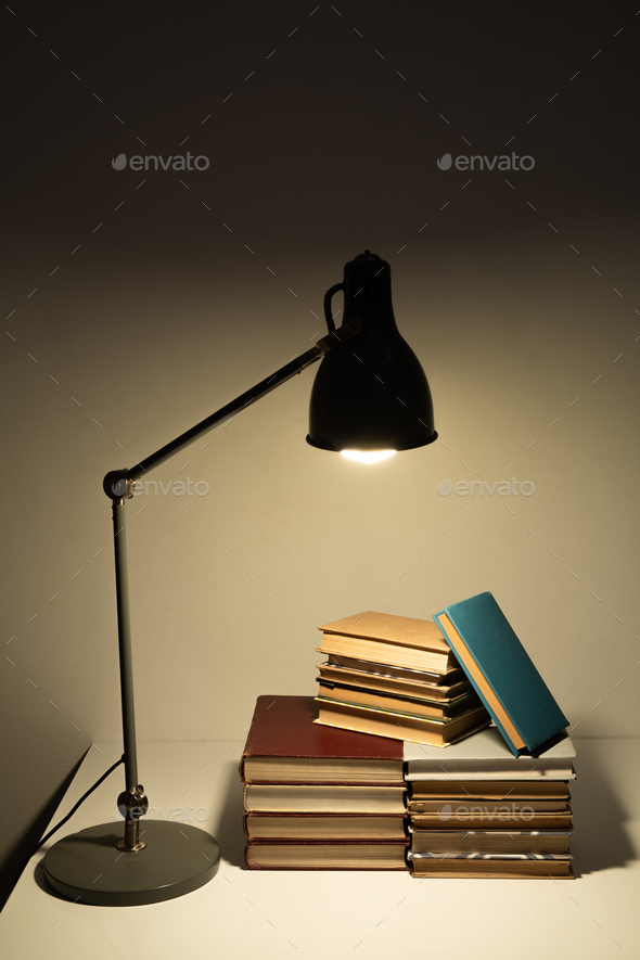 Light of lamp falling on pile of books or manuals of contemporary student