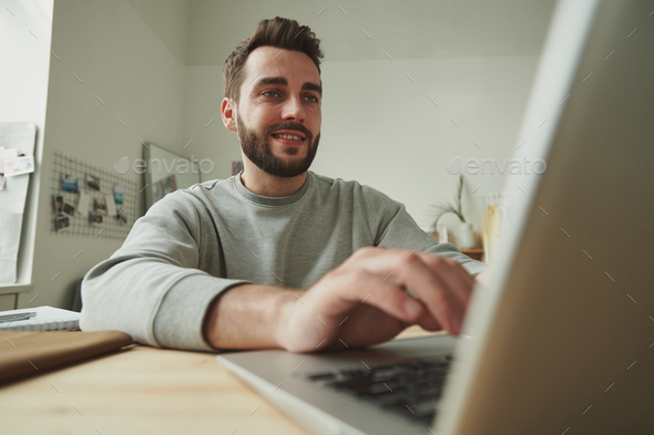 Smiling young businessman looking at laptop display while working remotely