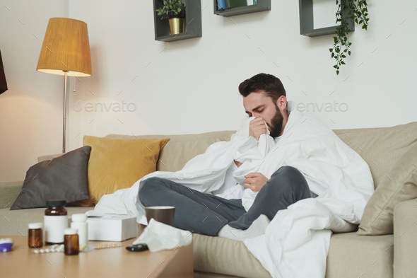 Sick man with flu or coronavirus sitting on couch in living-room and ...