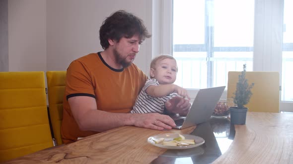 Alone Father Sits By the Laptop and His Little Baby Sits on His Knees and Pushing the Buttons alt