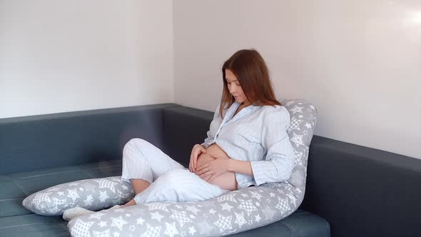 Happy pregnancy woman sitting on sofa at home and holding hands on belly
