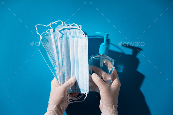 Woman hands in latex gloves holding facial medical masks and sanitizer, blue background - Stock Photo - Images