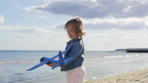 Happy Child Playing with a Toy Plane at the Beach During Summer Sunset. Girl Holds Airplane in Her